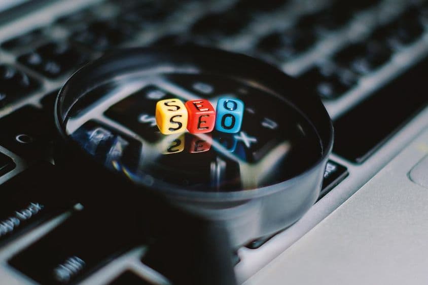 Egy hárombetűs "SEO" a nagyítón és a számítógép billentyűzetének hátterén.