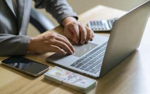 Könyvelő számológéppel és laptoppal végez pénzügyi számításokat.