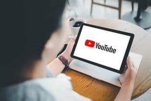 Egy nő egy kávézóban egy tabletet néz, a képernyőn YouTube látható.