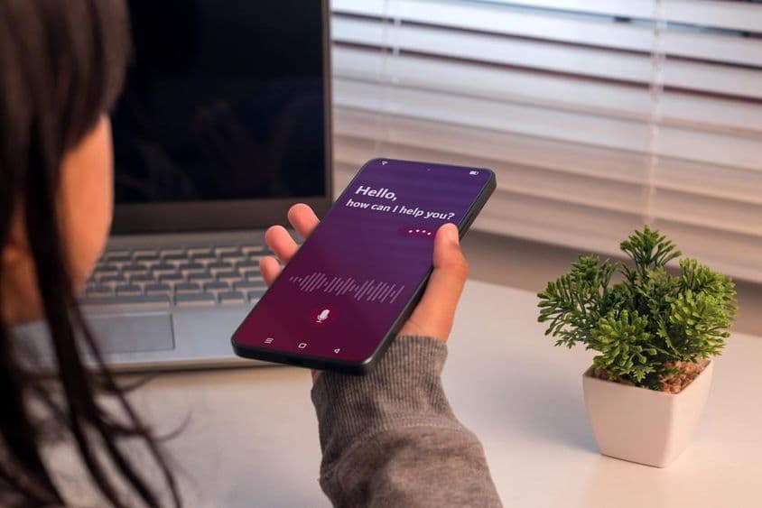 Egy fiatal lány okostelefon használ virtuális hang asszisztenst.